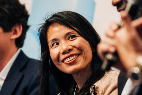 Vivian Wu smiles while seated on a panel and looking towards another speaker.