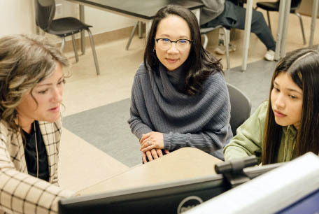 Two adults, including Sandra Liu Huang, look at a computer screen in a classroom with a student.